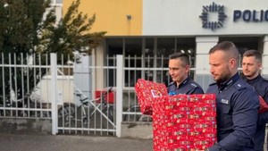 Policjanci niosą prezenty. W tle widać budynek Komendy Miejskiej Policji w Toruniu.