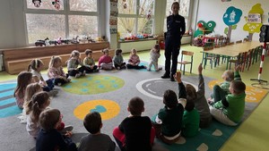 Na zdjęciu widzimy policjantkę wśród przedszkolaków. Policjantka rozmawia z grupą dzieci.