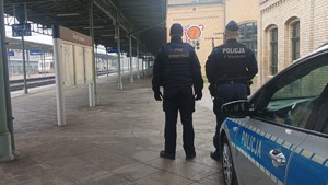 Na zdjęciach widać umundurowanego policjanta oraz funkcjonariusza Straży Ochrony Kolei na dworcu kolejowym Toruń Dworzec Główny. Policjant posiada założoną odblaskową kamizelkę koloru jaskrawo-żółtego z napisem "POLICJA". Na kolejnych zdjęciach policjant znajduje się w rejonie torów.