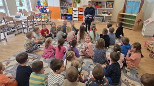 na zdjęciu widzimy dzieci oraz policjantkę wydziału ruchu drogowego. Policjantka omawia z dziećmi zasady bezpiecznego poruszania się po drodze.