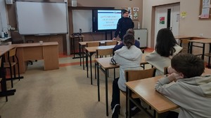 Na zdjęciu są profilaktycy na zajęciach z uczniami, podczas których omawiają tematykę bezpiecznych ferii, hejtu, przemocy rówieśniczej oraz narkotyków.