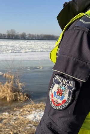 na zdjęciu widać umundurowanego funkcjonariusza policji, oznakowany radiowóz oraz zamarznięte akweny.