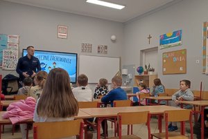 Zdjęcia przedstawiają dzielnicowego w trakcie spotkania z uczniami szkoły podstawowej. Dzieciom prezentowany jest radiowóz policyjny