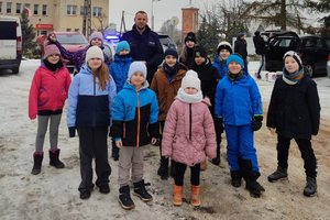 Zdjęcia przedstawiają dzielnicowego w trakcie spotkania z uczniami szkoły podstawowej. Dzieciom prezentowany jest radiowóz policyjny