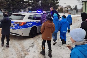 Zdjęcia przedstawiają dzielnicowego w trakcie spotkania z uczniami szkoły podstawowej. Dzieciom prezentowany jest radiowóz policyjny