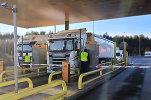 Na zdjęciu widać policjanta kontrolującego kierującego pojazdem ciężarowym w trakcie wjazdu na autostradę. Policjant posada założoną kamizelkę odblaskową.