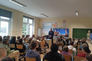 Na zdjęciach widoczny jest policjant w trakcie spotkania z uczniami szkoły podstawowej. Policjant jest w umundurowaniu służbowym. Na jednym ze zdjęć widać również fragment prezentowanego w trakcie zajęć filmu dot. bezpieczeństwa w Internecie.