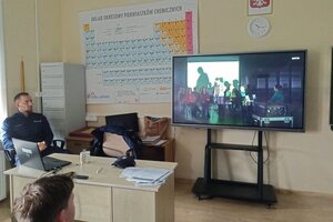 Na zdjęciach widoczny jest policjant w trakcie spotkania z uczniami szkoły podstawowej. Policjant jest w umundurowaniu służbowym. Na jednym ze zdjęć widać również fragment prezentowanego w trakcie zajęć filmu dot. bezpieczeństwa w Internecie.