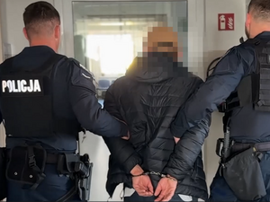 Na zdjęciu widać zatrzymanego mężczyznę, którego prowadzi dwójka umundurowanych funkcjonariuszy policji.