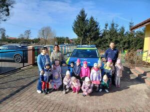 Na zdjęciach widać umundurowanych funkcjonariuszy policji. Prowadzą zajęcia w grupie przedszkolaków. Na jednym ze zdjęć grupa dzieci jest przy oznakowanym policyjnym radiowozie. Kolejne zdjęcia przedstawiają dzieci w trakcie zajęć.