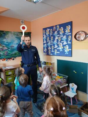 Na zdjęciach widać umundurowanych funkcjonariuszy policji. Prowadzą zajęcia w grupie przedszkolaków. Na jednym ze zdjęć grupa dzieci jest przy oznakowanym policyjnym radiowozie. Kolejne zdjęcia przedstawiają dzieci w trakcie zajęć.