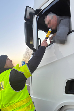 Na dwóch zdjęciach widać umundurowanego funkcjonariusza Policji, dokonującego badania stanu trzeźwości kierujących. Trzecie zdjęcie przedstawia pojazd dostawczy, który umieszczany jest na lawecie.