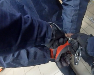 policjant zakłada mężczyźnie kajdanki na ręce trzymane z tyłu