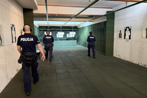 na zdjęciu widać policjantów poruszających się na krytej strzelnicy w trakcie zawodów.