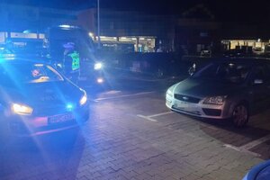 Zdjęcie wykonane w porze nocnej. Widać na nim kontrolowany pojazd oraz radiowóz policji z włączonymi światłami błyskowymi.