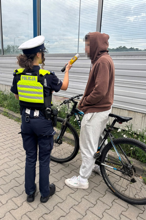 Na zdjęciu znajduje się umundurowana policjantka ruchu drogowego oraz kierujący rowerem, wobec którego podejmowane są czynności. Policjantka dokonuje sprawdzenia stanu trzeźwości.