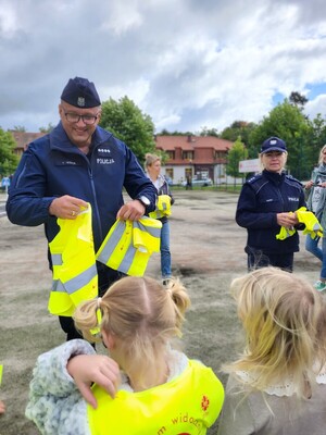 na zdjęciach znajdują się przedstawiciele Policji oraz innych służb mundurowych w trakcie przekazywania odblaskowych kamizelek dzieciom.
