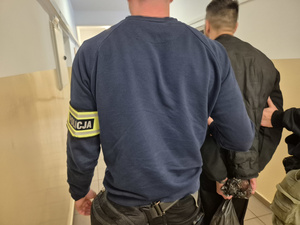 na zdjęciu znajduje się nieumundurowany policjant prowadzący zatrzymanego mężczyznę